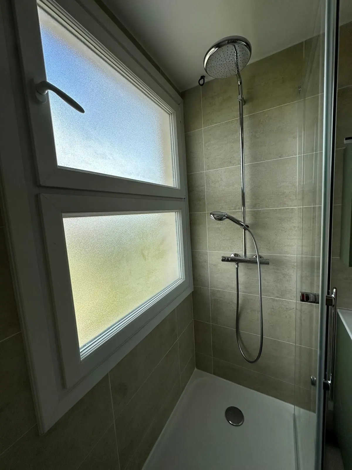 Douche vitrée et meuble vasque devant une fenêtre